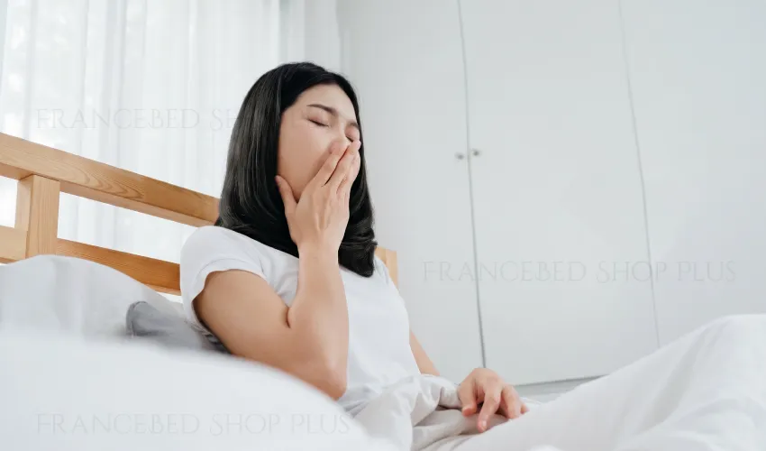 眠くなり、ベッドの上であくびをしている女性